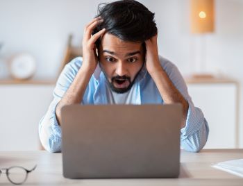 Frustrated man looking at laptop screen and touching head in shock